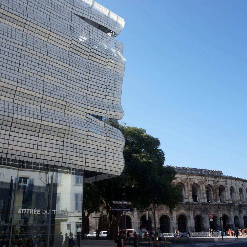 vue de la façade du musée de la romanité avec les arènes de Nîmes en arrière plan