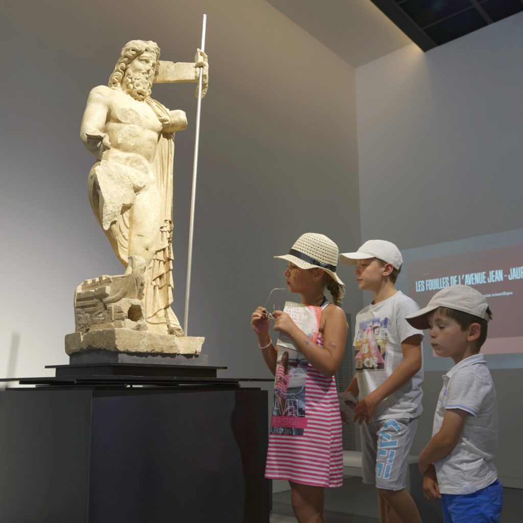 trois enfants regardent une statue représentant Neptune