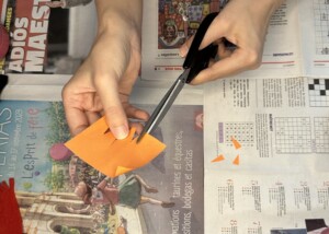 Main qui découpe un carré de papier orange